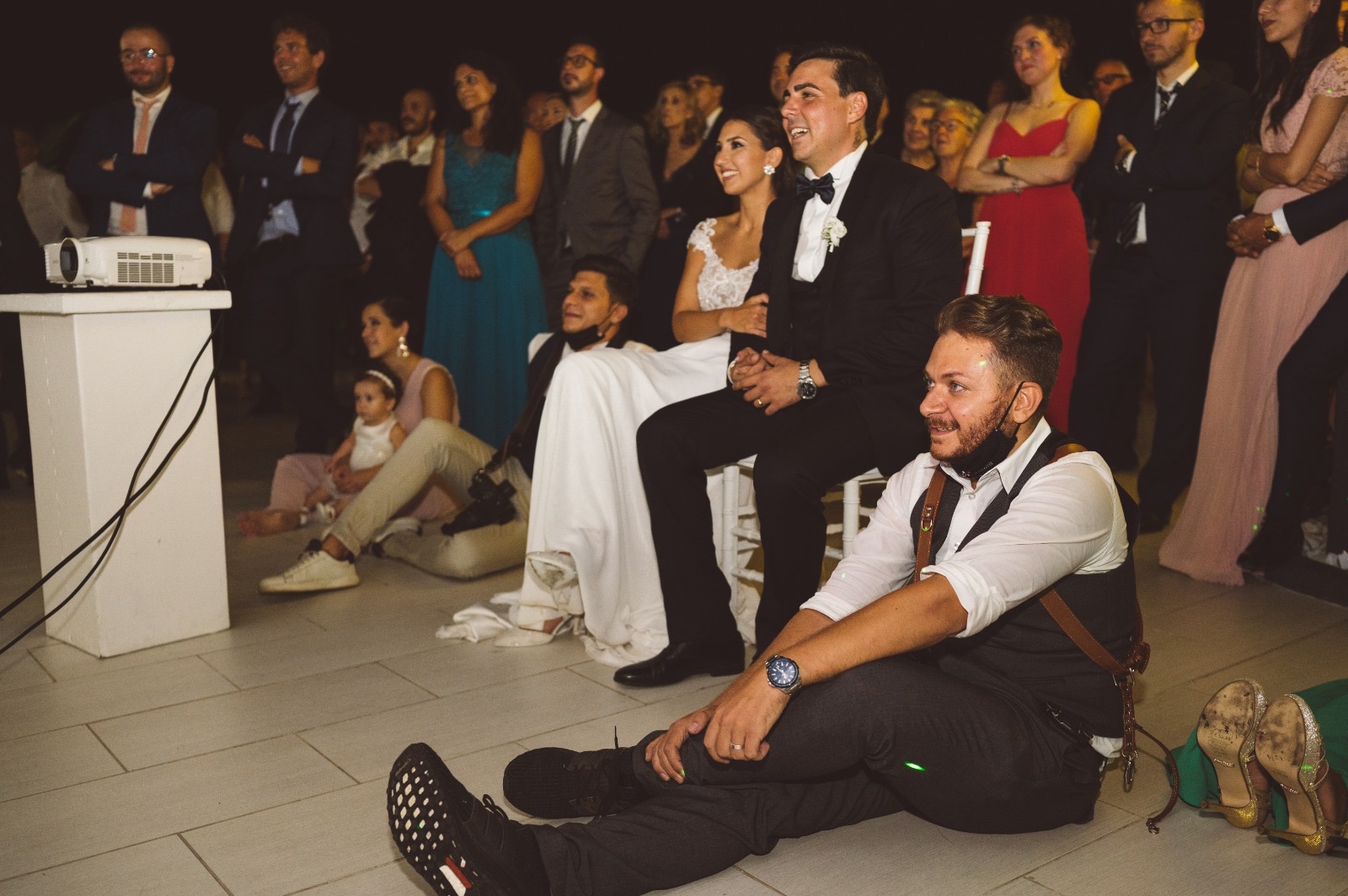 The bride and groom and their guests watching the same day edit on screen, with Giuseppe Cimino sitting on the floor beside them