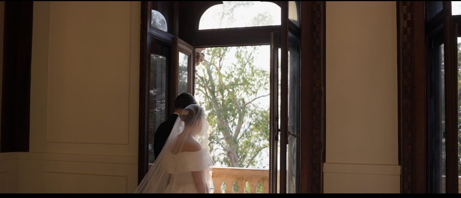Bride and groom stepping through the doors of a historic Italian villa, backlit